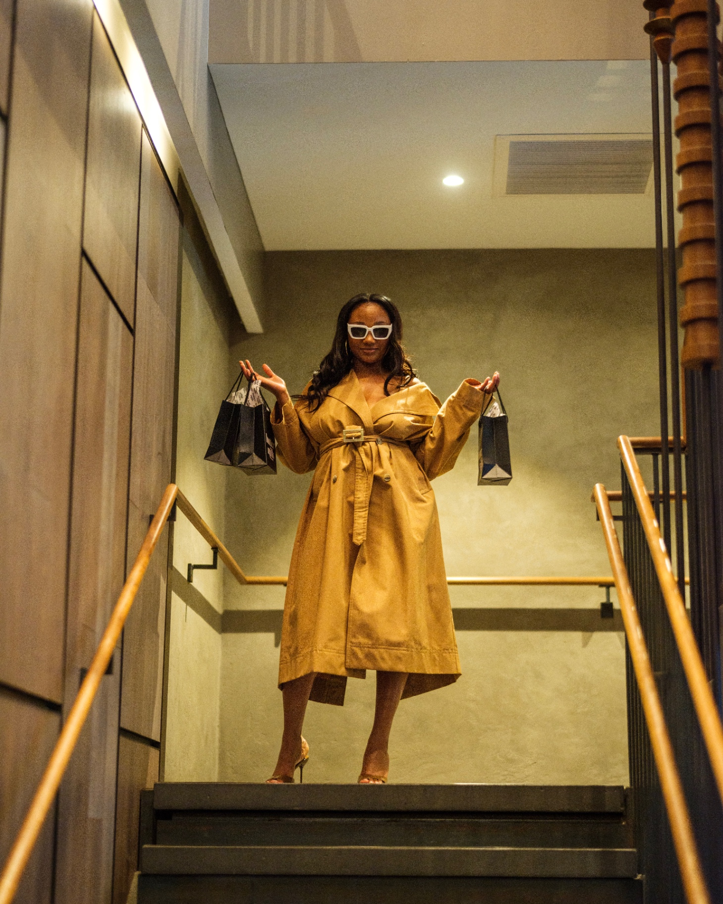 Model in camel trench on steps holding Buttermilk Balm gift bags