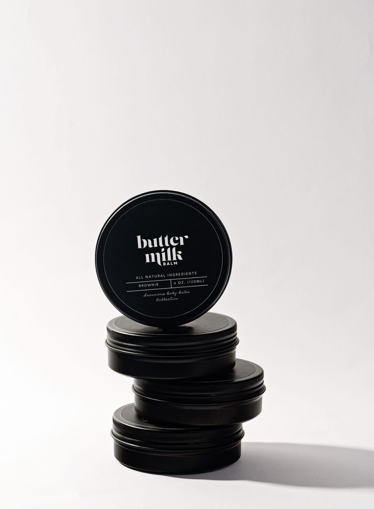 Stack of Brownie Buttermilk Balm tins in soft studio light